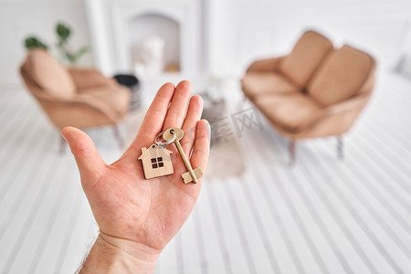家里的门摄影照片_男人手拿着钥匙与房子形状的钥匙扣。