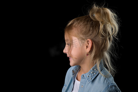 一个沉思的小女孩的侧面肖像。在黑色背景上。