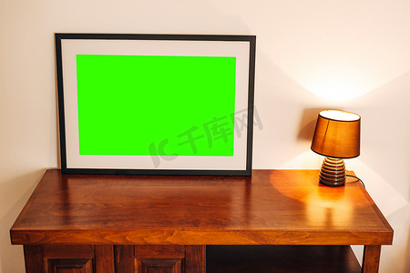 木插图摄影照片_黑框中的空画矗立在木桌上，靠近发光的夜灯