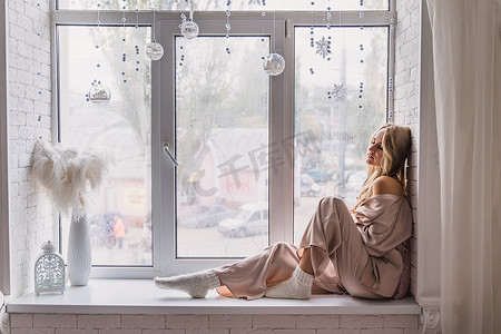 穿着睡衣坐在家里窗台上休息和思考的女人。