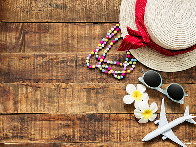 花朵海报摄影照片_帽子、项链、太阳镜、花朵和红心形的平躺式作为暑假旅行的配饰，以及带有复制空间的木制背景平面模型。