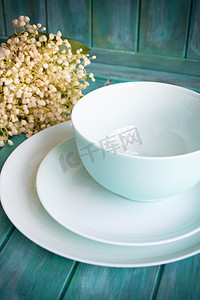 春季餐桌布置，配有复古蓝色蓝绿色餐具和蓝绿色木质背景上的山谷百合花束。