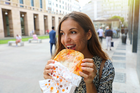 快乐的年轻女商人在短暂的午休时间吃一个小披萨。