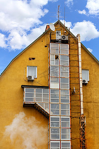 一栋老房子，房子的底部有一个玻璃防火梯，映衬着蓝天白云。