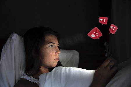 年轻漂亮的女人躺在床上，拿着智能手机，在社交媒体上收到互联网成功概念的点赞和评论，在白床单上看到顶视图