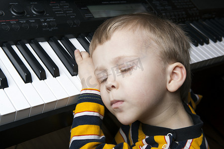 懒惰的孩子摄影照片_坐在钢琴前睡觉的小男孩
