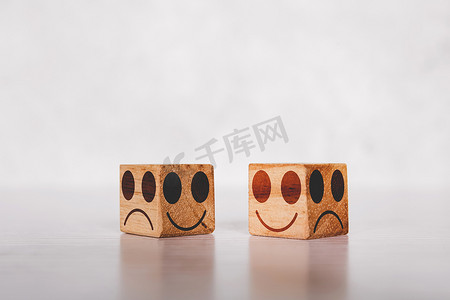 发呆表情包摄影照片_立方体木块上的面部表情，带有关于真诚和坦率的情感和表达，带有桌子上的隐喻，象征着积极的微笑和快乐的概念，消极或虚假的不快乐。