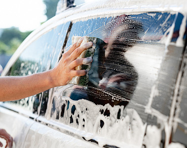 窗户泡沫摄影照片_用海绵清洗车窗的手