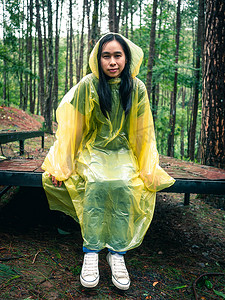 鹿黄色摄影照片_穿着黄色雨衣的快乐亚洲女人坐在木鹿上