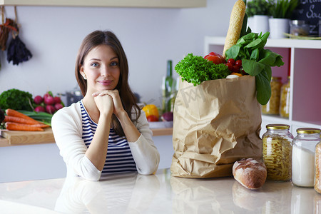 年轻女子拿着蔬菜购物袋。站在厨房里。