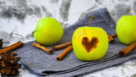 金苹果摄影照片_绿色金苹果或史密斯奶奶心形切在苹果上，肉桂棒放在厨房毛巾上，准备食物，甜点