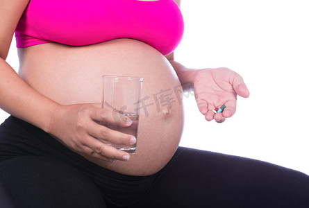 孕妇手的特写镜头，背景是一杯水和药丸