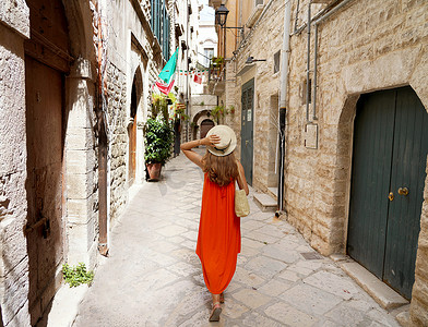意大利普利亚比谢列中世纪历史小镇狭窄小巷中穿着橙色夏长裙的妇女