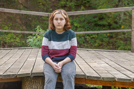 短发少女摄影照片_初秋时节，一个留着短发的少女坐在大自然的长木凳上，直视前方