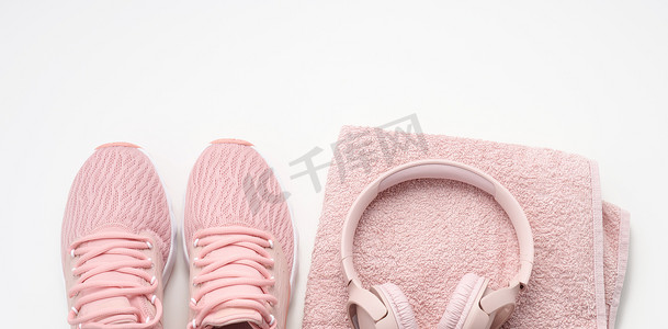 白色背景上的一双粉色纺织运动鞋、无线耳机和一条粉色纺织毛巾