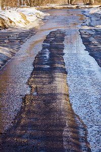 冰雪场景摄影照片_用冰雪覆盖的冬季道路，有水坑和车辙