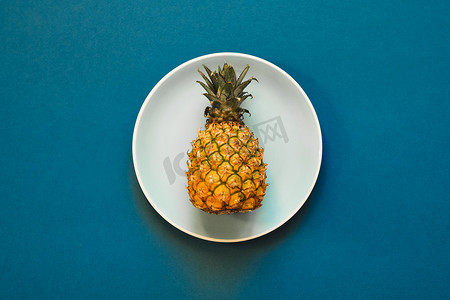 平铺菠萝摄影照片_在蓝色背景板上的小菠萝。