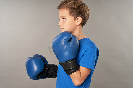 拳击可爱摄影照片_戴着拳击手套的可爱男孩站在灰色背景下