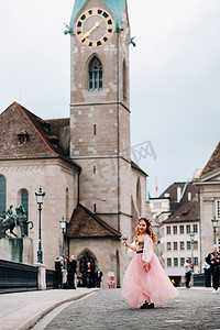 一个穿着粉色公主裙、手里拿着花束的小女孩走过苏黎世老城。瑞士城市街道上一个穿着粉色裙子的女孩的肖像