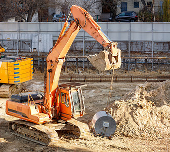 重型履带式施工挖掘机在市区居民楼之间的围栏建筑工地上工作。