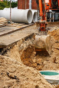 一辆重型建筑挖掘机的铲斗在修理道路上的城市收集器时挖了一条沟渠。
