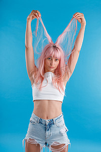 穿着休闲装的有趣女模特玩着粉红色的头发，把头发举过头顶，孤立地站在蓝色工作室背景上