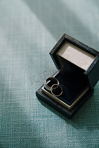 金色结婚戒指装在黑色盒子里，放在有图案的织物上。