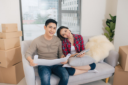 年轻的亚洲夫妇坐在沙发上，看着新家的蓝图。