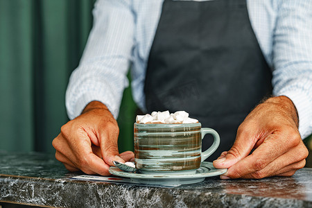 咖啡师的手端着一杯用棉花糖装饰的热可可饮料