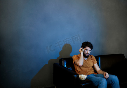 孤独的男人坐在沙发上，手里拿着爆米花盘灰墙