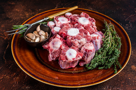 牛骨头摄影照片_新鲜未煮过的牛肉牛尾切肉在质朴的盘子上，配上香草。