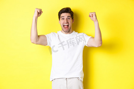 黄色加油摄影照片_兴奋的男子获胜、举手庆祝、胜利并为团队加油的形象，站在黄色背景上