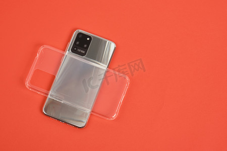 现代智能手机，配有 3 个摄像头、金属机身和红色背景顶视图上的透明硅胶外壳