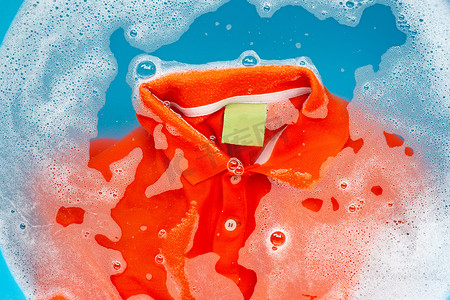 洗衣粉摄影照片_橙色polo衫泡在洗衣粉水中溶解，洗