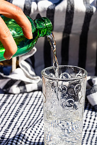 透明玻璃瓶子摄影照片_将水从绿色瓶子倒入玻璃杯中