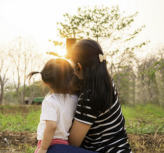 女孩与母亲合影摄影照片_亚洲小女孩在日落背景下在花园里与母亲合影的后视图。