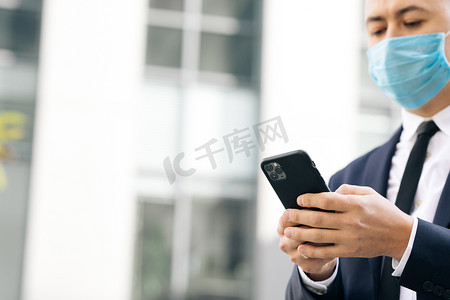 小程序摄影照片_街上戴着防护面罩的男子看着智能手机浏览社交媒体应用程序。