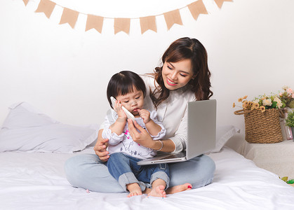 经典名著摄影照片_穿着经典西装的亚洲女士在家里用笔记本电脑工作，她的女婴与父亲聊天。