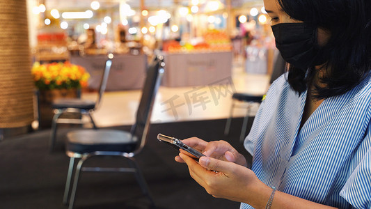 智能食堂摄影照片_在商店里使用智能手机和坐在分开的椅子上的亚洲女性