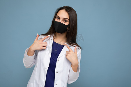 脸上戴着病毒防护面罩的黑发阳性女性，可抵御冠状病毒，蓝色背景中隔离有白色医用外套