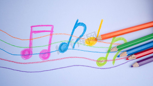 彩色铅笔创意艺术摄影照片_彩色铅笔放在白皮书背景上，上面有音乐笔记图画。