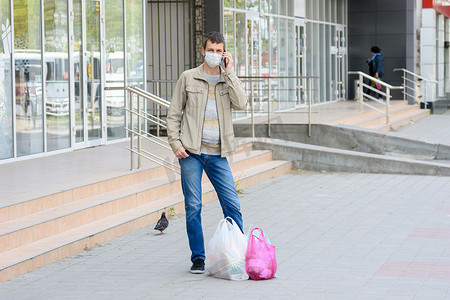 一个戴医用口罩的男人站在街上购物，用手机说话
