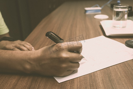 一个忙碌的商人的手在办公桌上用笔在一张纸上写字的侧视图。