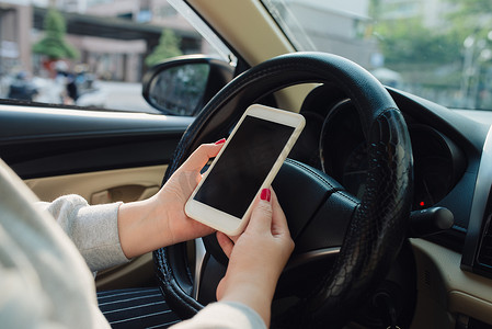 驾驶汽车离开家时使用带空白屏幕的移动智能手机的女性手的模型图像。