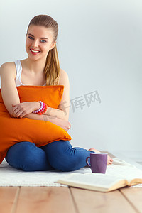 年轻女子坐在枕头上，手里拿着一杯茶