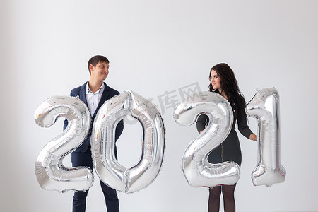 2021快乐摄影照片_新年、庆祝和节日概念 — 情侣在白色背景下用银气球制成的2021年标志玩得开心