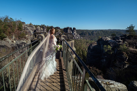 瑞士萨克森、德国巴斯泰山峡谷背景下，一位身穿白色连衣裙、一束鲜花的新娘