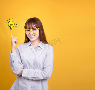 海报广告创意摄影照片_戴着黄色复古眼镜的亚洲女商人站着，指尖上有创意的灯泡灯，黄色背景，带有用于设计海报和广告文字的复制空间。 