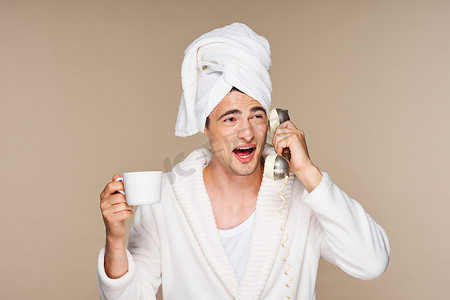 一个头上戴着毛巾的男人正在打电话，手里拿着一杯咖啡