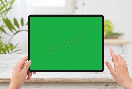绿色模板摄影照片_孤立的人左手拿着带白色绿色屏幕模型和厨房木桌的黑色平板媒体设备